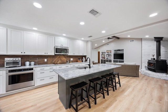 kitchen with stainless steel appliances, a sink, open floor plan, visible vents, and a wood stove