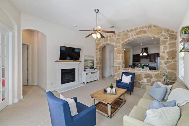 living room featuring a ceiling fan, a fireplace with raised hearth, arched walkways, light carpet, and visible vents