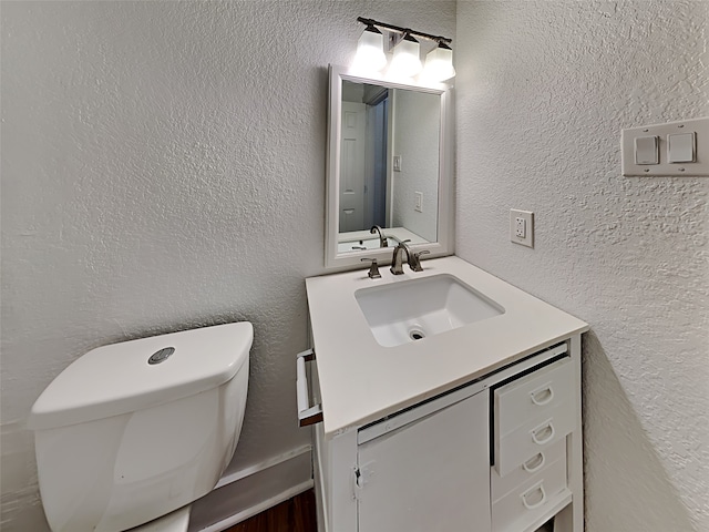 half bath with a textured wall, vanity, and toilet