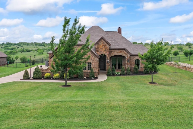 tudor home featuring a chimney, brick siding, fence, stone siding, and a front lawn