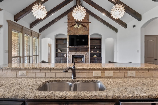 kitchen with high vaulted ceiling, a sink, beamed ceiling, a large fireplace, and light stone counters