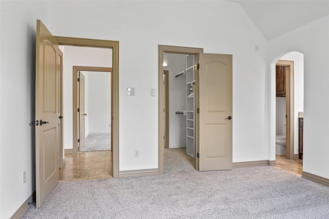 unfurnished bedroom featuring light carpet, a walk in closet, and arched walkways