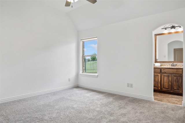 unfurnished bedroom featuring lofted ceiling, light carpet, connected bathroom, and baseboards