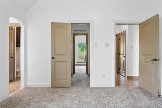 unfurnished bedroom with light carpet, arched walkways, and baseboards