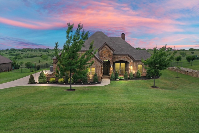 french provincial home with a chimney, a yard, brick siding, fence, and stone siding