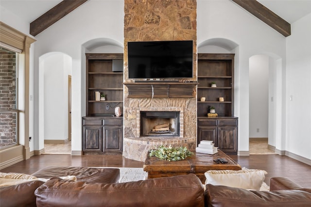 living area featuring wood finished floors, beam ceiling, built in features, arched walkways, and a stone fireplace