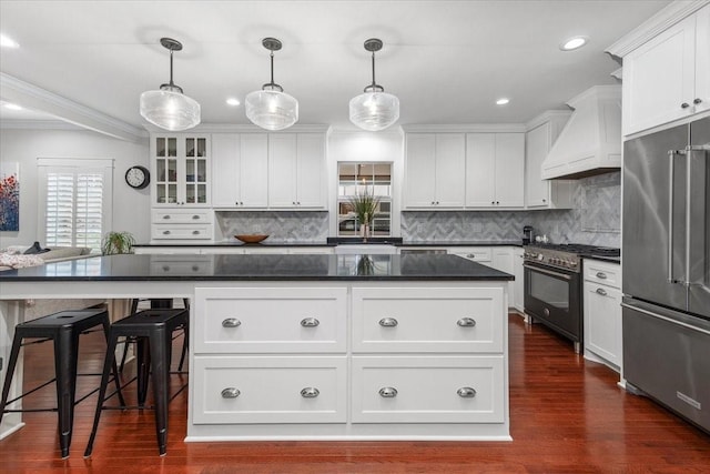 kitchen featuring high end appliances, custom range hood, ornamental molding, a kitchen island, and white cabinetry