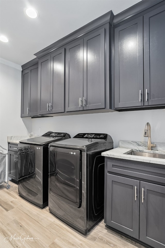 washroom with a sink, separate washer and dryer, cabinet space, light wood finished floors, and ornamental molding