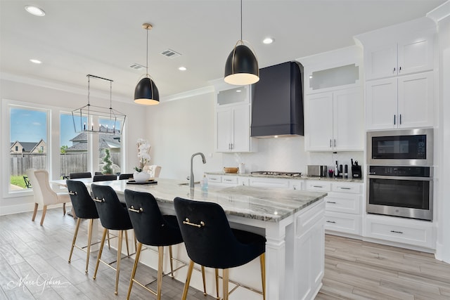 kitchen with tasteful backsplash, appliances with stainless steel finishes, wall chimney exhaust hood, white cabinetry, and visible vents