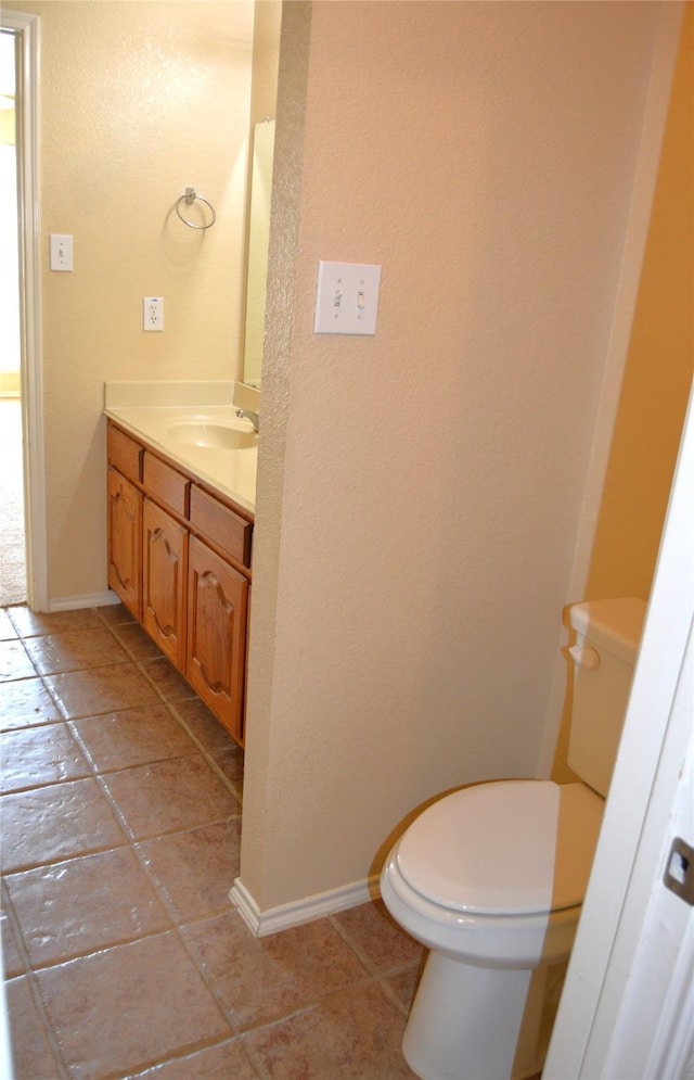 half bath with baseboards, vanity, tile patterned flooring, and toilet