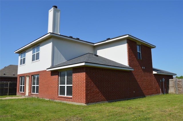 back of property with brick siding, a chimney, fence, and a yard