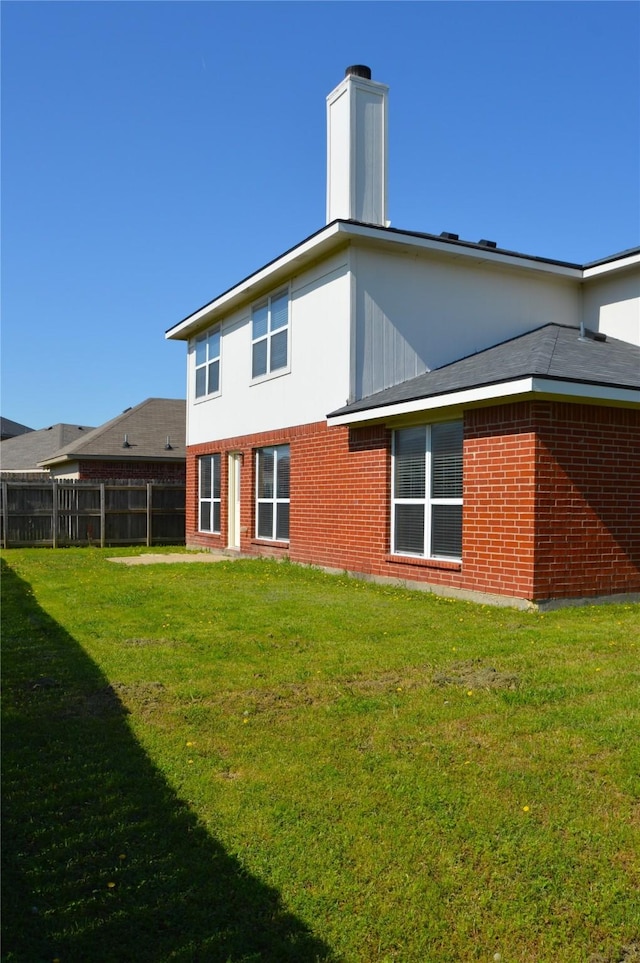 rear view of house featuring a lawn, brick siding, fence, and a chimney