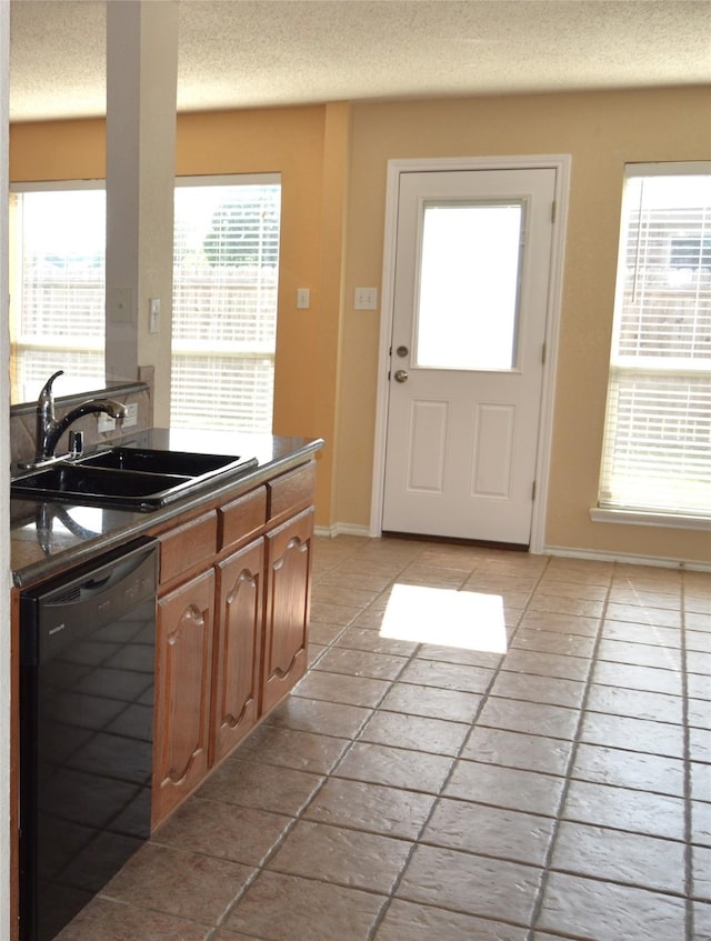 kitchen featuring a sink, a textured ceiling, dark countertops, baseboards, and black dishwasher