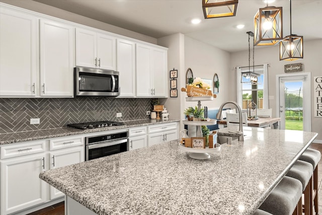 3912 Burks Ct, Celina, TX 75009 - kitchen featuring stainless steel appliances, a center island with sink, white cabinetry, tasteful backsplash, and light stone counters