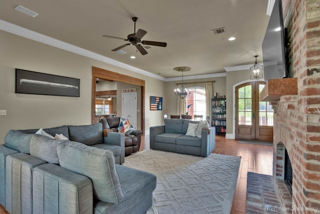 living area with a wealth of natural light, crown molding, wood finished floors, and ceiling fan with notable chandelier