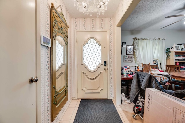 entryway featuring light tile patterned flooring, wallpapered walls, and ceiling fan with notable chandelier