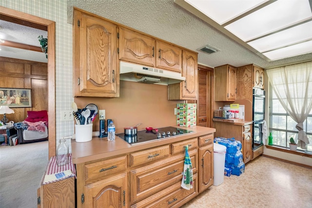 kitchen with black electric cooktop, under cabinet range hood, double wall oven, light countertops, and a textured ceiling