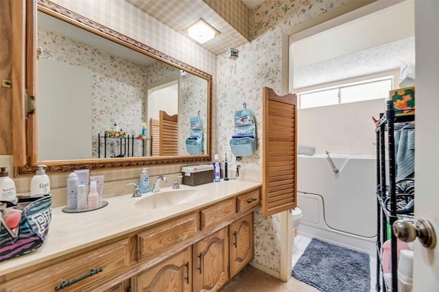 bathroom with a washtub, toilet, vanity, and wallpapered walls