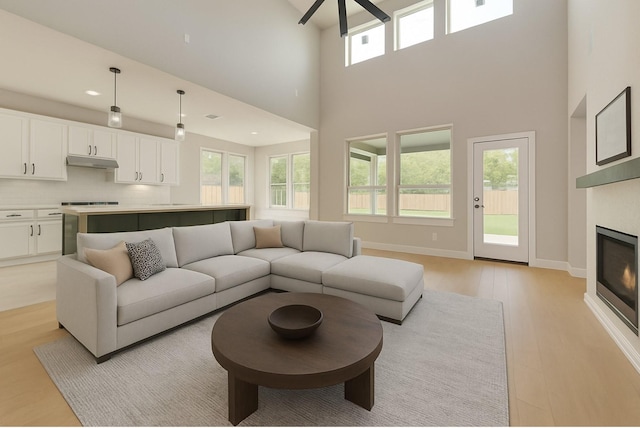 6810 Windward View Dr, Rowlett, TX 75088 - living room featuring light wood-style floors, a towering ceiling, a glass covered fireplace, a ceiling fan, and baseboards
