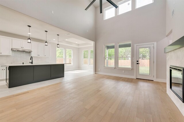 6810 Windward View Dr, Rowlett, TX 75088 - unfurnished living room featuring a glass covered fireplace, light wood-style flooring, a high ceiling, a sink, and healthy amount of natural light