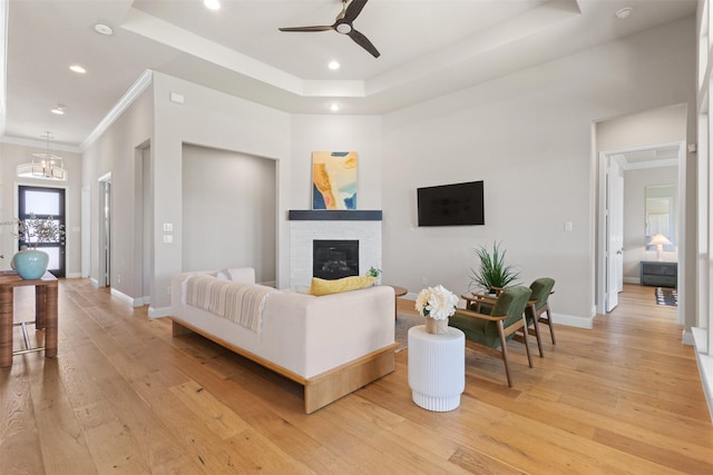 living area featuring ceiling fan, light wood-style floors, and a raised ceiling