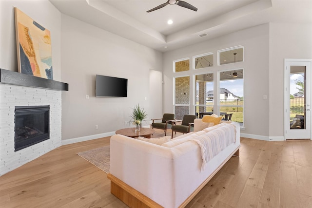 living area featuring a tray ceiling, visible vents, a fireplace, light wood-style flooring, and ceiling fan