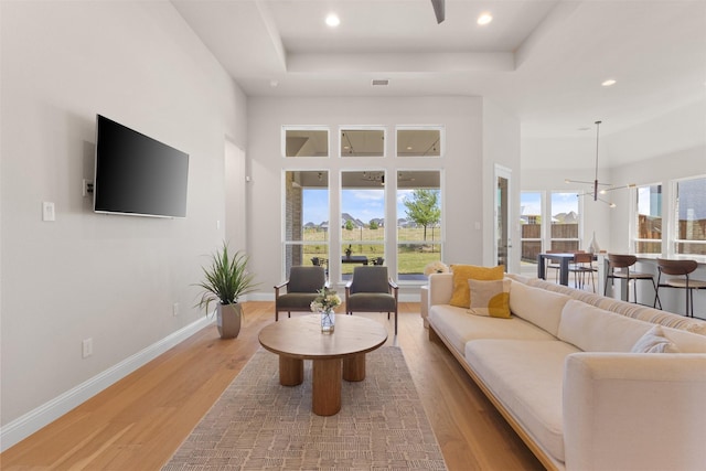 living area with a raised ceiling, visible vents, light wood finished floors, and recessed lighting