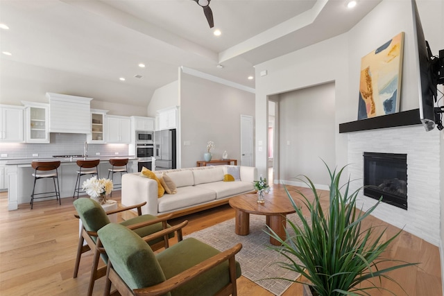 living area with high vaulted ceiling, a glass covered fireplace, light wood finished floors, and recessed lighting