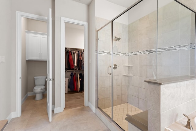 bathroom with a shower stall, a walk in closet, baseboards, toilet, and tile patterned flooring