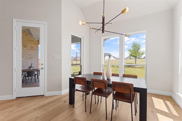 dining space with light wood-style floors, lofted ceiling, baseboards, and a notable chandelier