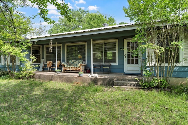 rear view of house with a lawn, covered porch, and metal roof