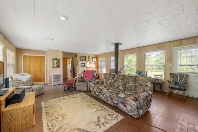 living area with brick patterned floor, wooden walls, a wood stove, and heating unit