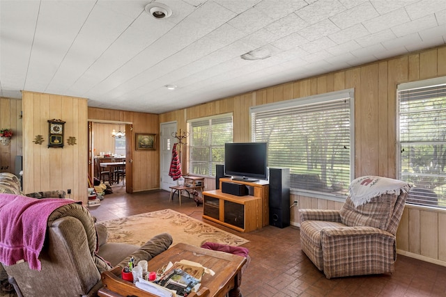 living room featuring wood walls, brick floor, and an inviting chandelier