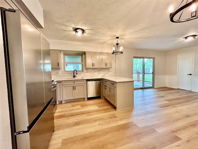 kitchen with a sink, light wood-style floors, an inviting chandelier, stainless steel appliances, and a peninsula