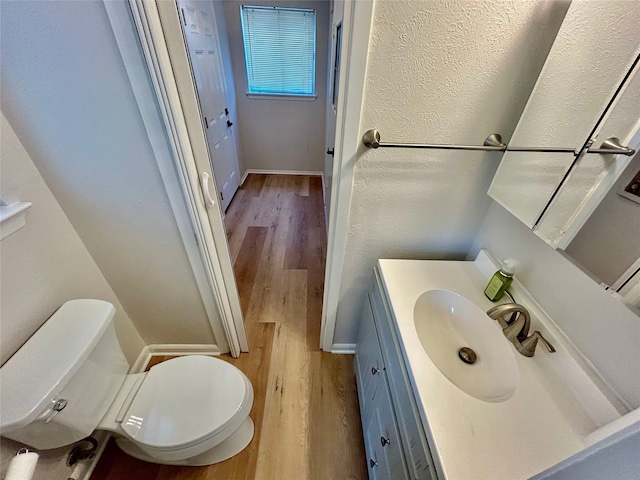 half bathroom with wood finished floors, toilet, and vanity