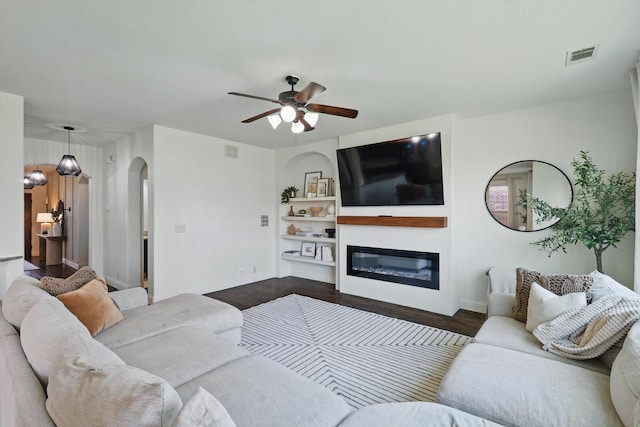 1308 Kittyhawk Dr, Little Elm, TX 75068 - living room featuring arched walkways, dark wood-style flooring, a glass covered fireplace, and a ceiling fan