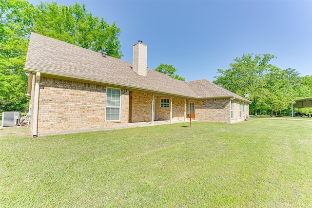 back of house with a chimney, brick siding, central AC, a yard, and a shingled roof