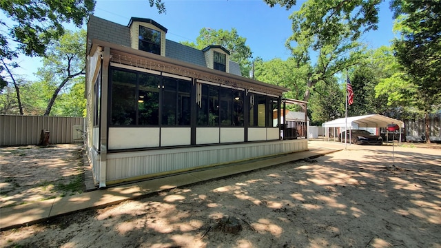 rear view of house featuring a detached carport, fence, a sunroom, and mansard roof