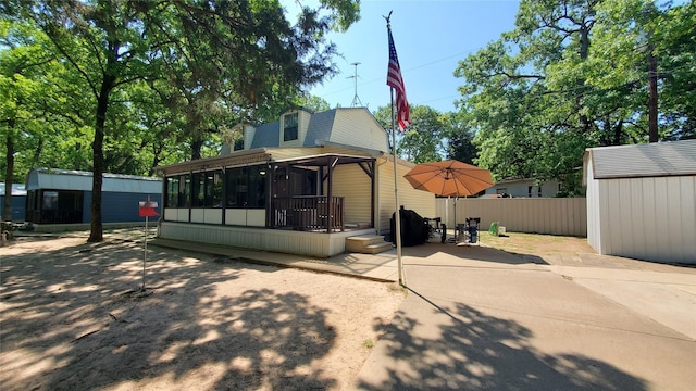 rear view of house with a storage shed, an outbuilding, fence, a sunroom, and a patio