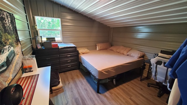 bedroom with vaulted ceiling, light wood-style flooring, and wood walls