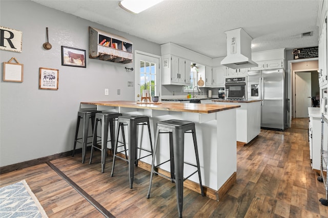 kitchen with dark wood-style floors, butcher block counters, black oven, a peninsula, and stainless steel refrigerator with ice dispenser
