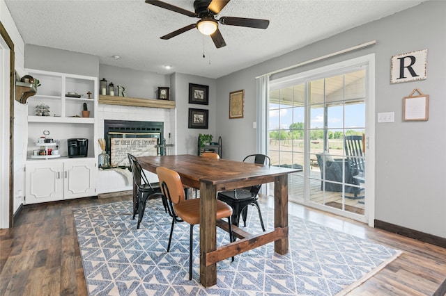 dining space with ceiling fan, dark wood-style flooring, a glass covered fireplace, and a textured ceiling
