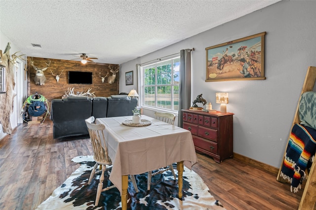 dining space with wood finished floors, visible vents, a ceiling fan, an accent wall, and a textured ceiling