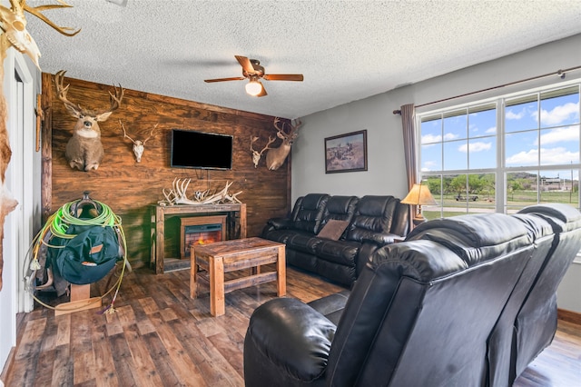 living room with wood finished floors, a textured ceiling, a ceiling fan, and a large fireplace