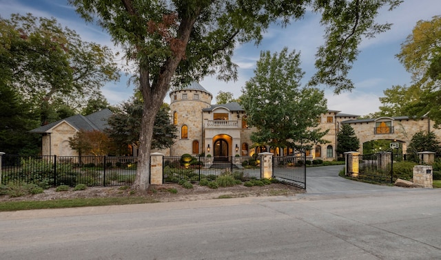 mediterranean / spanish-style home featuring stone siding, driveway, a gate, and a fenced front yard