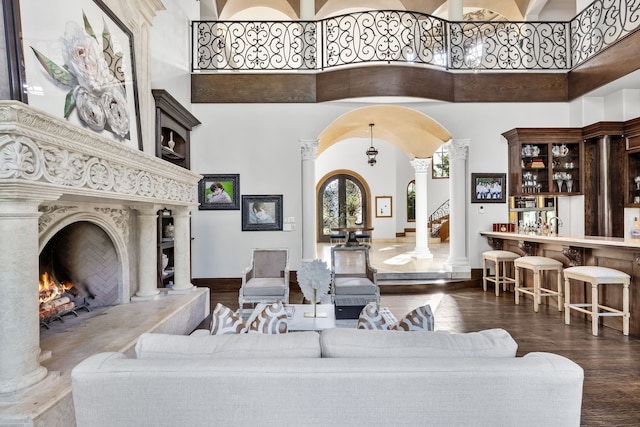 living room with arched walkways, ornate columns, a premium fireplace, wood finished floors, and a high ceiling