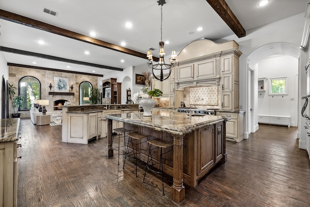 kitchen with arched walkways, beam ceiling, a spacious island, and cream cabinets