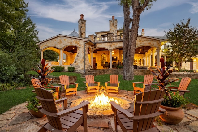back of property with a patio, a balcony, stone siding, and an outdoor fire pit
