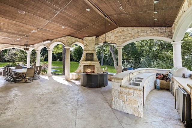 view of patio with an outdoor stone fireplace, outdoor dining space, an outdoor kitchen, and ceiling fan