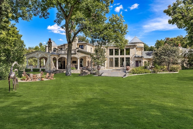 rear view of property with stone siding, a lawn, a balcony, and a patio